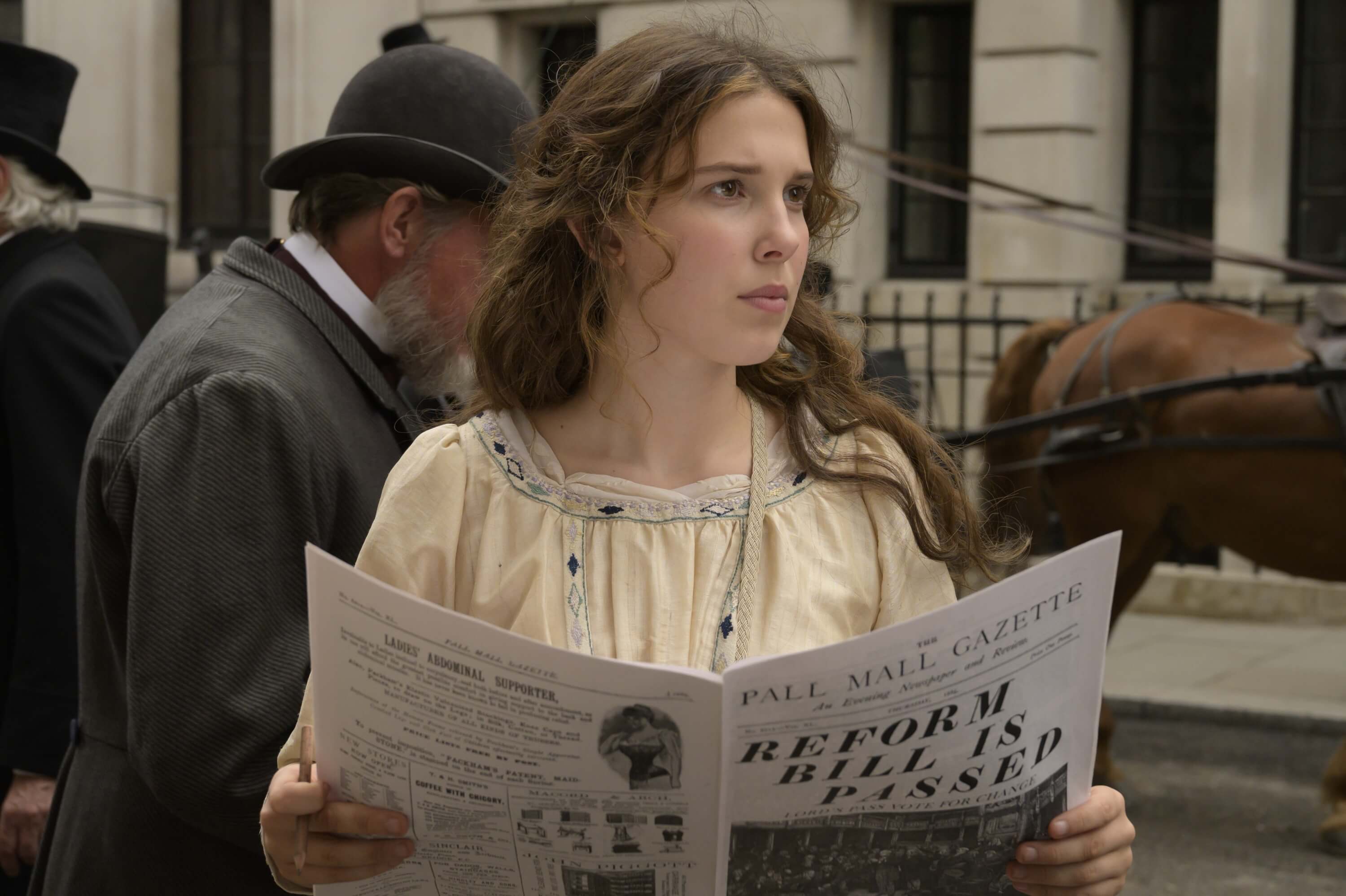 Millie Bobby Brown as Enola Holmes reading newspaper