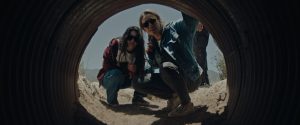 Promotional shot from the 2026 film Redux Redux showing Irene and Mia studying the entrance to a smuggler's underground lair